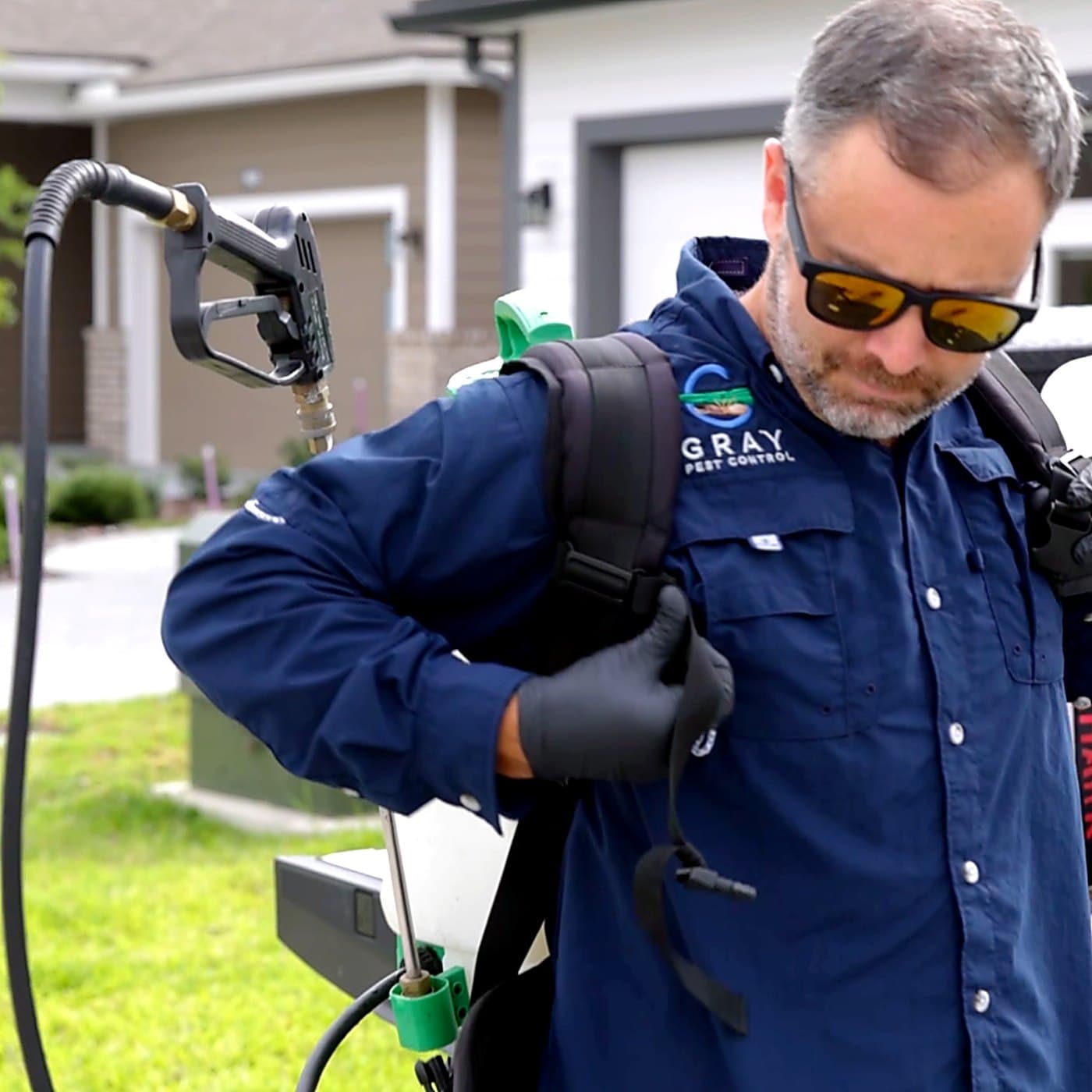 Gray Pest Control technician with a backpack sprayer in front of a Northeast Florida home